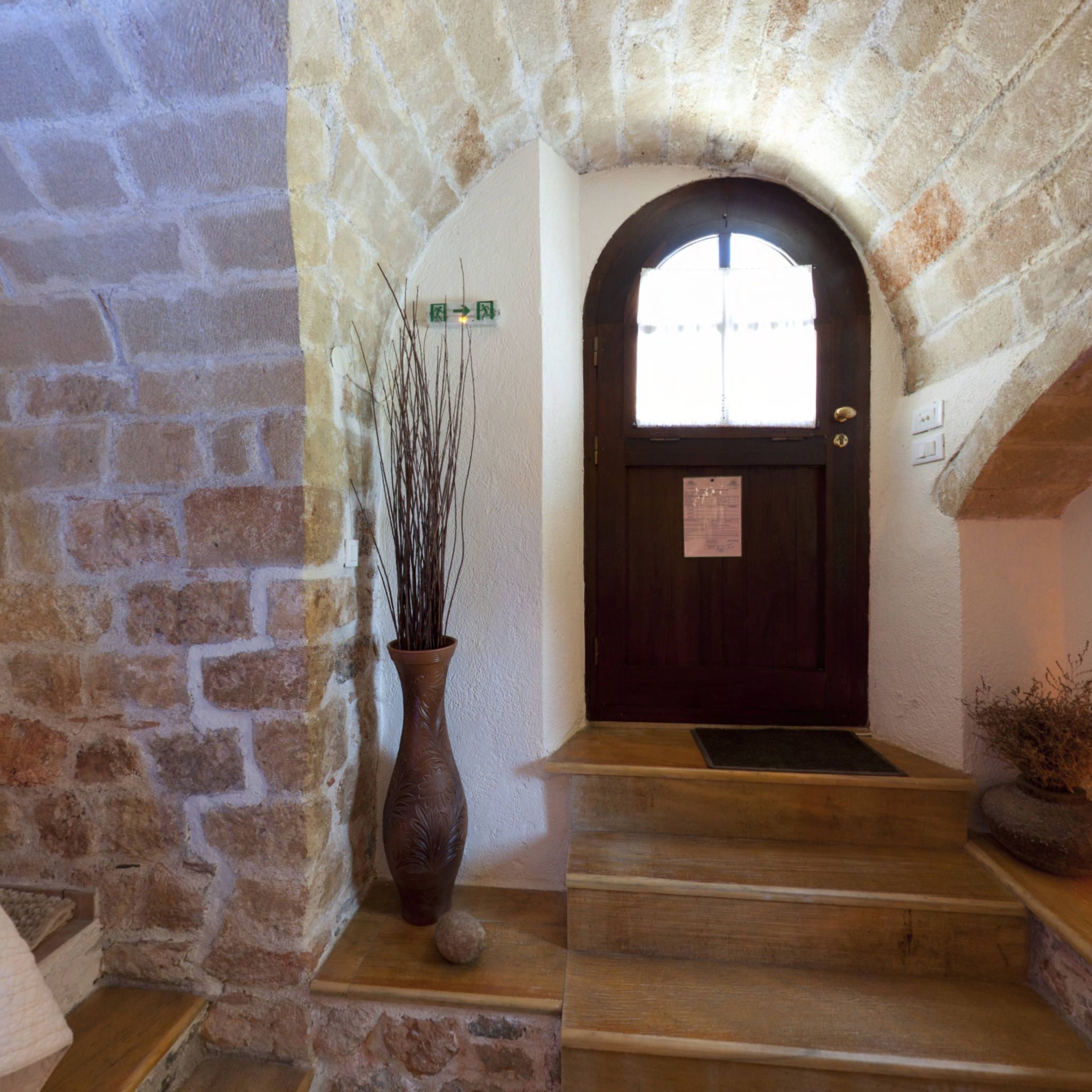 A stone staircase leading to a dark wooden door with a window above it. A decorative vase with branches is placed on the steps.