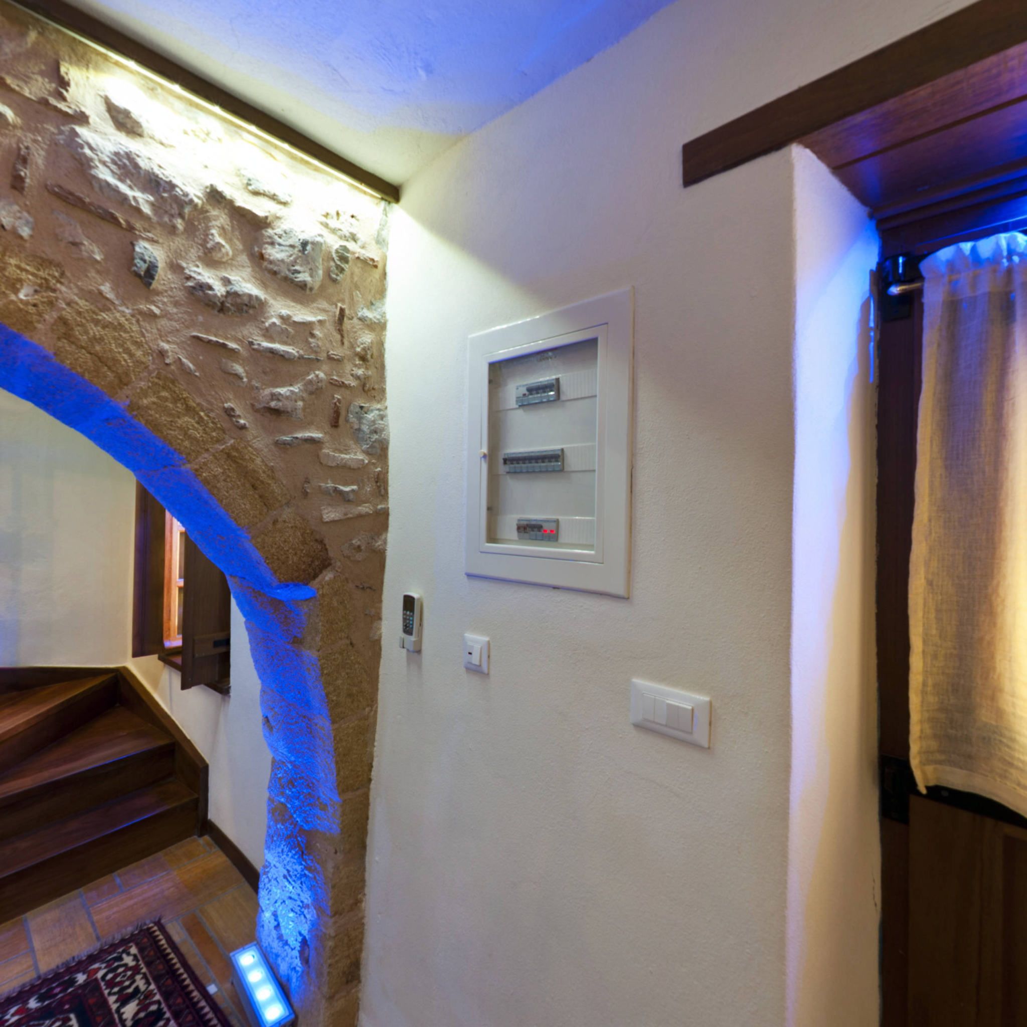 A staircase with a stone wall, a light switch, and a thermostat on the wall.