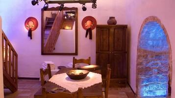 A dining area with a table set for two, a wooden cabinet, a mirror, and a stone wall with blue lighting.