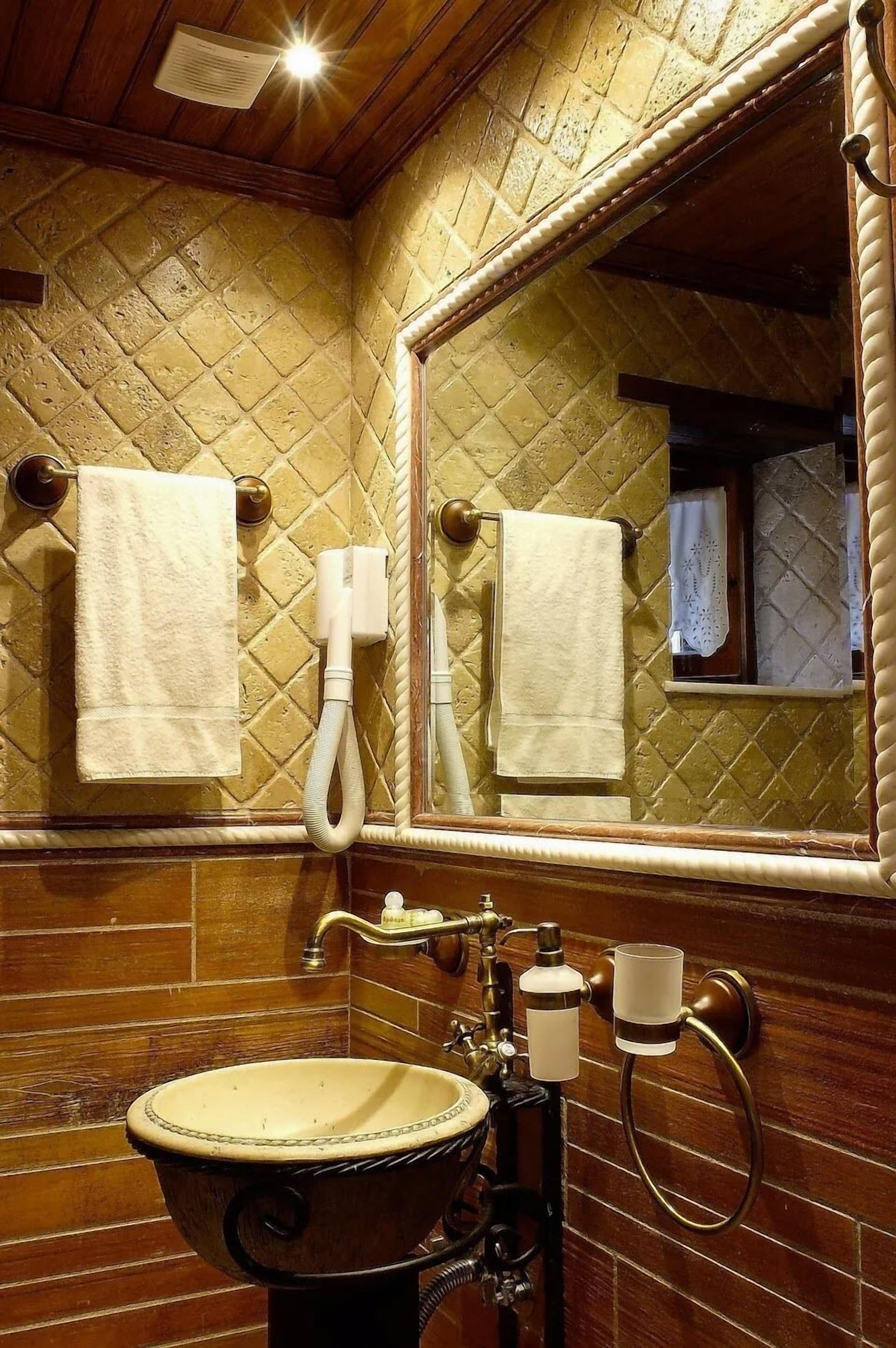 Un baño con un lavabo antiguo, un espejo grande y dos toallas colgadas en la pared.