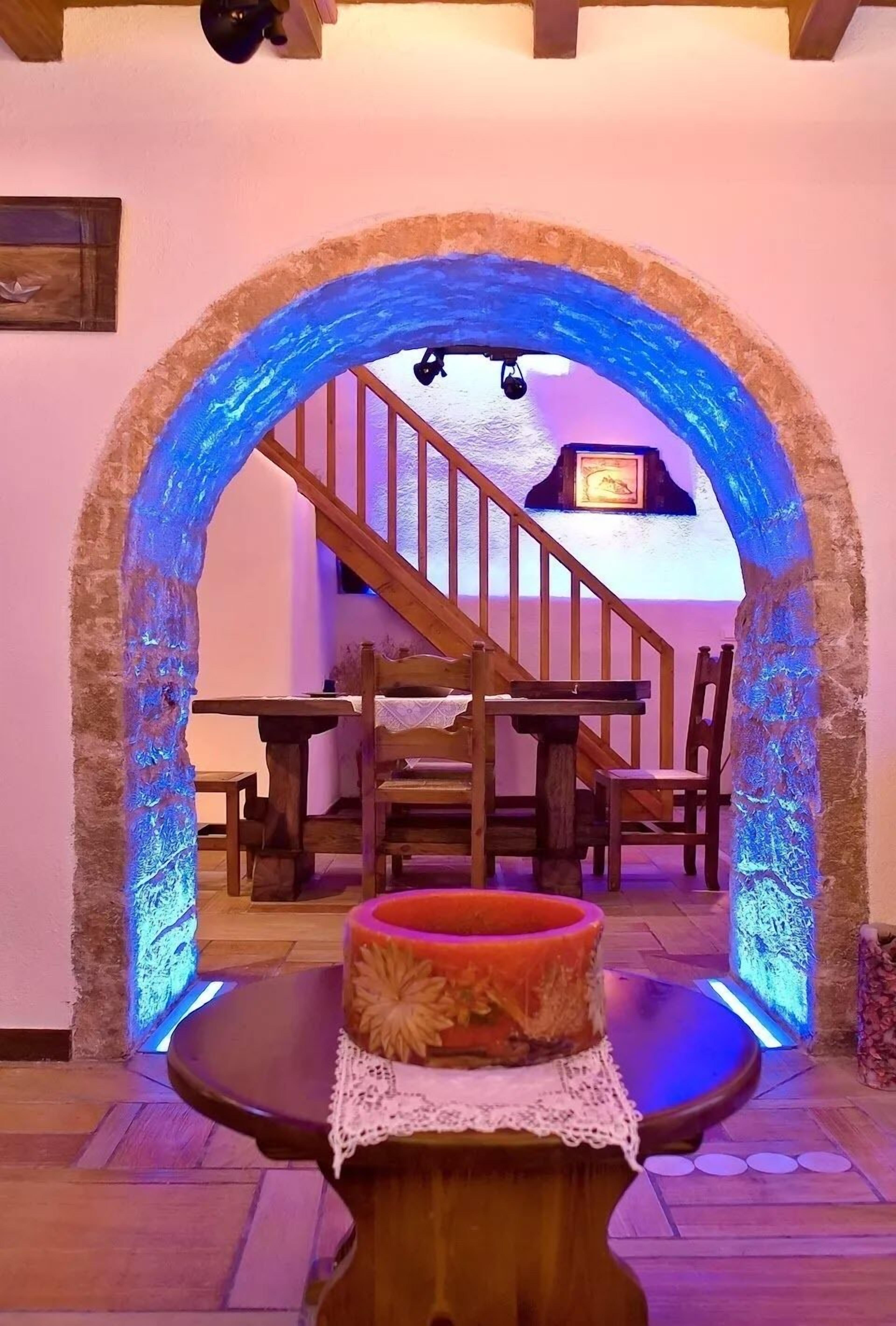 Un interior con una escalera de madera, una zona de comedor y una mesa con cojín.