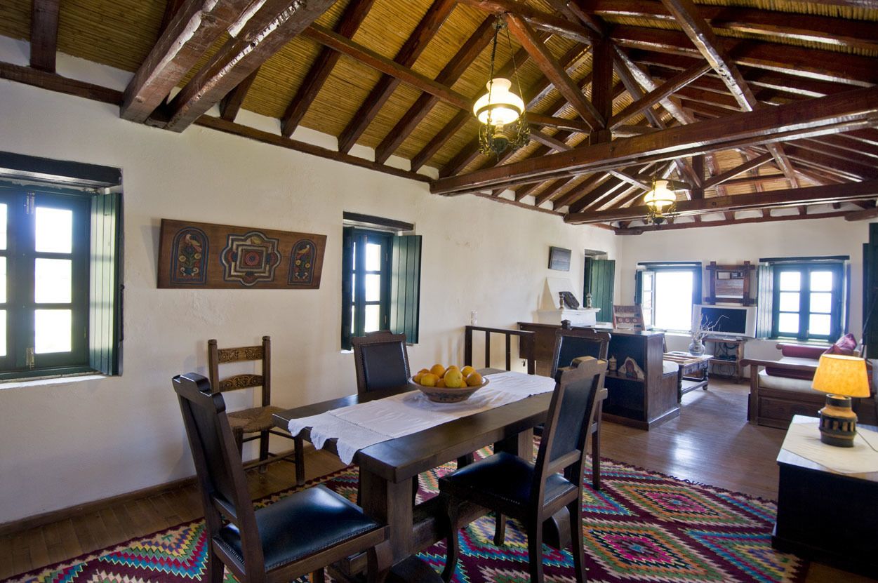 A dining area with a wooden table and chairs, a fruit bowl, and a patterned rug.