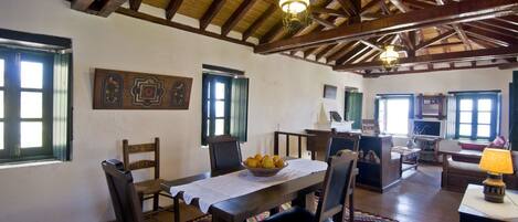 A dining area with a wooden table and chairs, a fruit bowl, and a patterned rug.