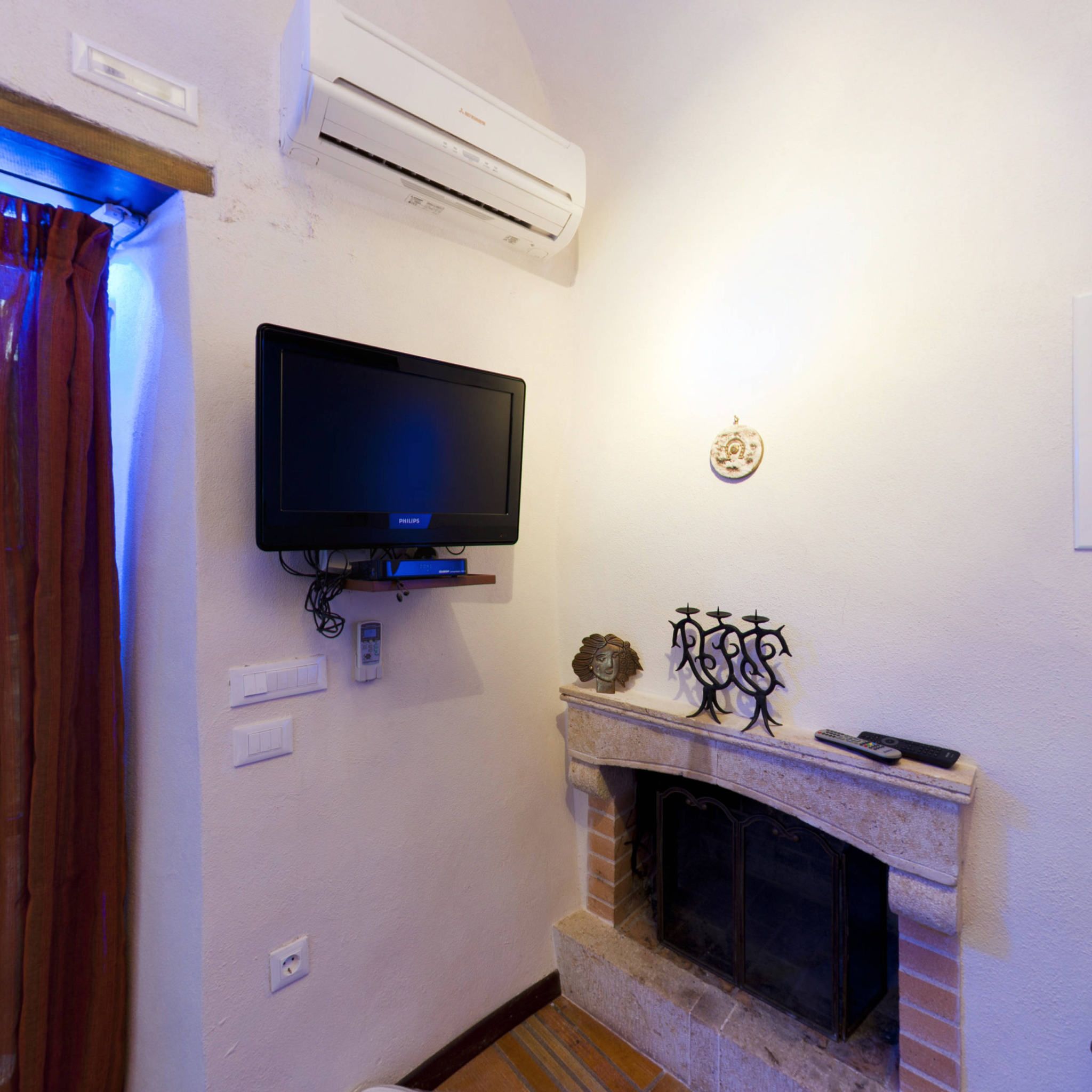 A living room with a mounted flat-screen TV, a fireplace with a mantel, and an air conditioning unit above the TV.
