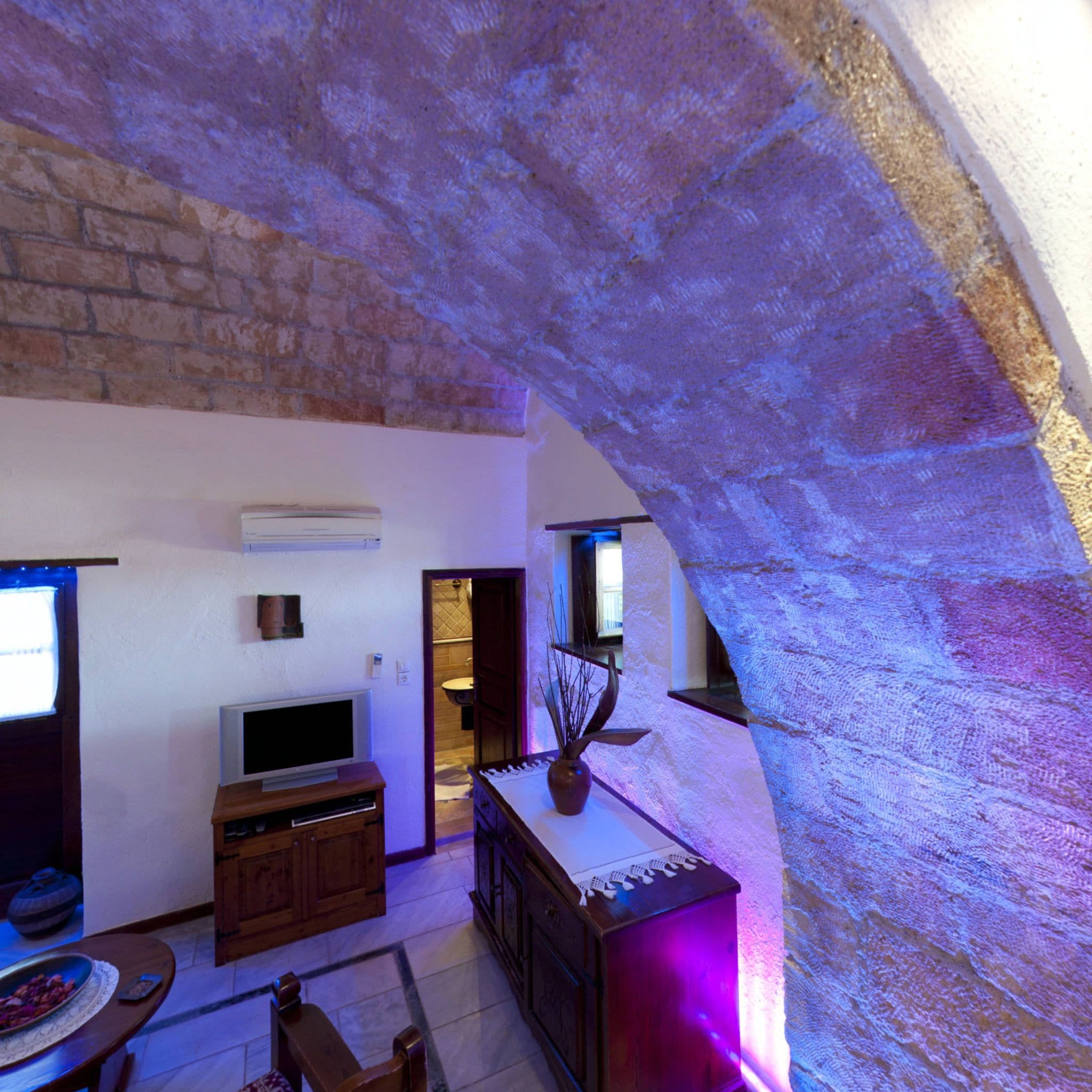 A room with a stone archway, a television, wooden furniture, and a plant.