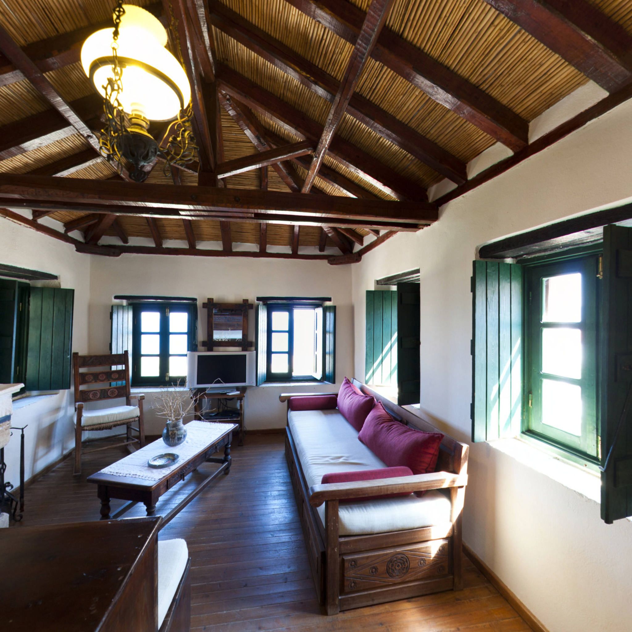 A room with a wooden ceiling, a sofa, a television, and a table with a vase.
