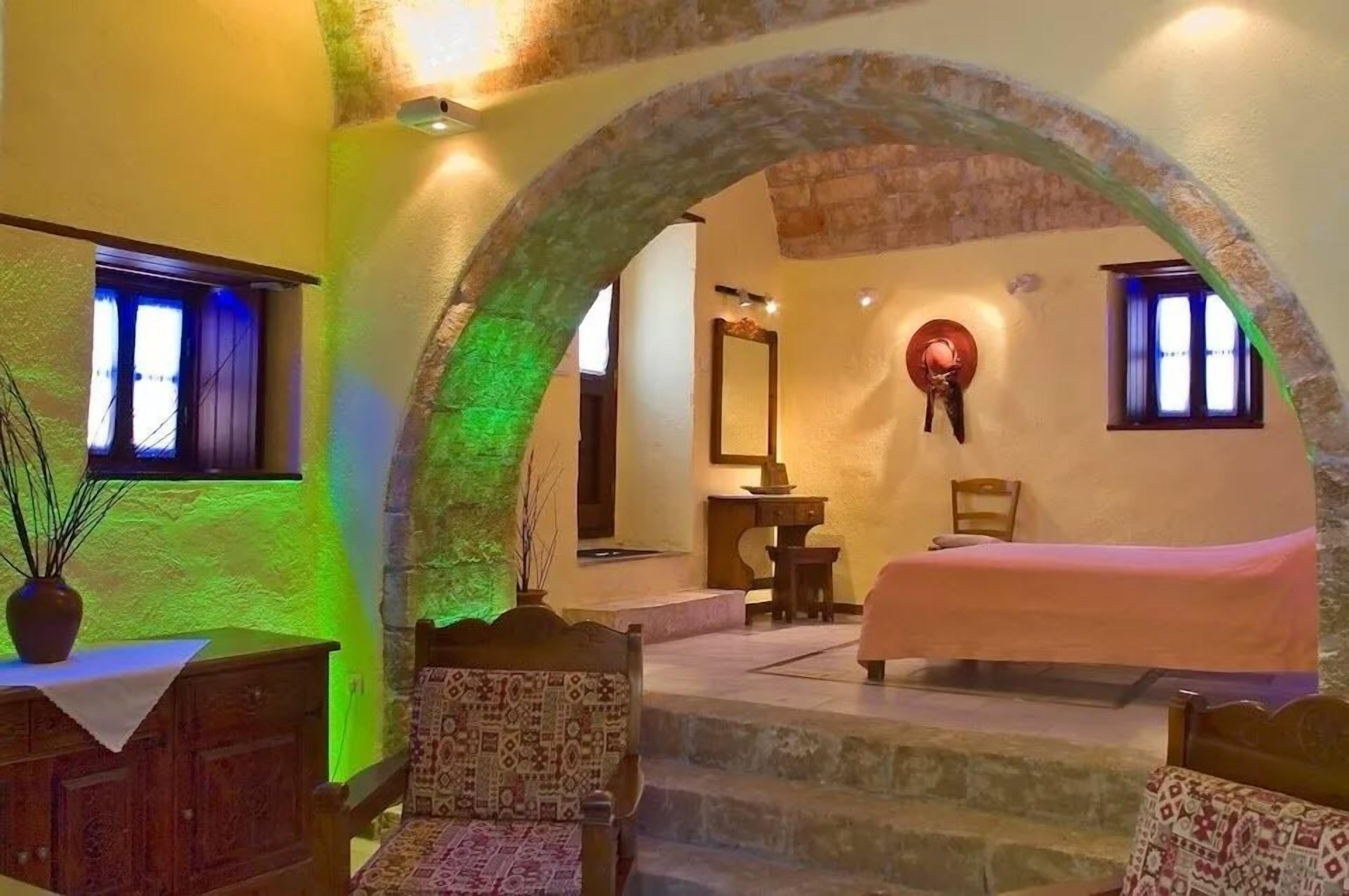 Una habitación acogedora con cama, escritorio y silla. Se observa un arco de piedra y una ventana con luz azul.