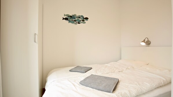 A bedroom with a bed, pillows, a wall art piece, and a bedside lamp.