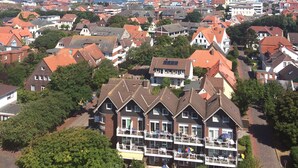 A residential area with a mix of houses and apartment buildings, featuring a prominent red-roofed building with a balcony and a view of the sea. - Ferienwohnung Leuchtturmblick (Wangerooge)