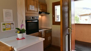 A compact kitchen with wooden cabinets, a built-in oven, and a window overlooking a mountainous landscape. - Grand Cap 4 - Appt 4 pers in Chalet - CALM & NATURE (Tignes)