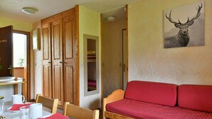 A room with a wooden bed, a red sofa, a dining table with plates and glasses, and a wall-mounted deer painting. - Grand Cap 4 - Appt 4 pers in Chalet - CALM & NATURE (Tignes)