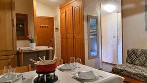 A dining area with a table set for four, a red pot on a stand, and a wooden door in the background. - CHALET LE GRAND CAP 7 (Tignes)