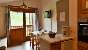 A cozy room with a wooden bench, a dining table with chairs, a small kitchen area with a coffee maker, and a TV on the wall. - CHALET LE GRAND CAP 7 (Tignes)
