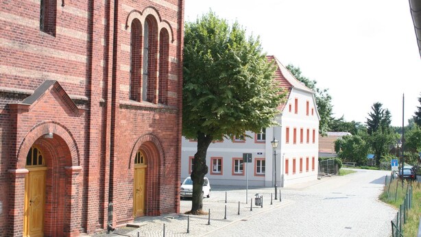 A red brick building with arched doorways and a tree in front. - Ferienwohnungen Peitz (Peitz)