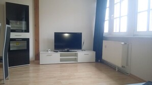 A modern living room with a flat-screen TV on a white entertainment unit, a built-in oven, and a radiator. - Ferienwohnungen Peitz (Peitz)