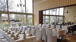 A dining area with multiple tables set for a meal, large windows, and a chandelier. - Ferienwohnungen Peitz (Peitz)