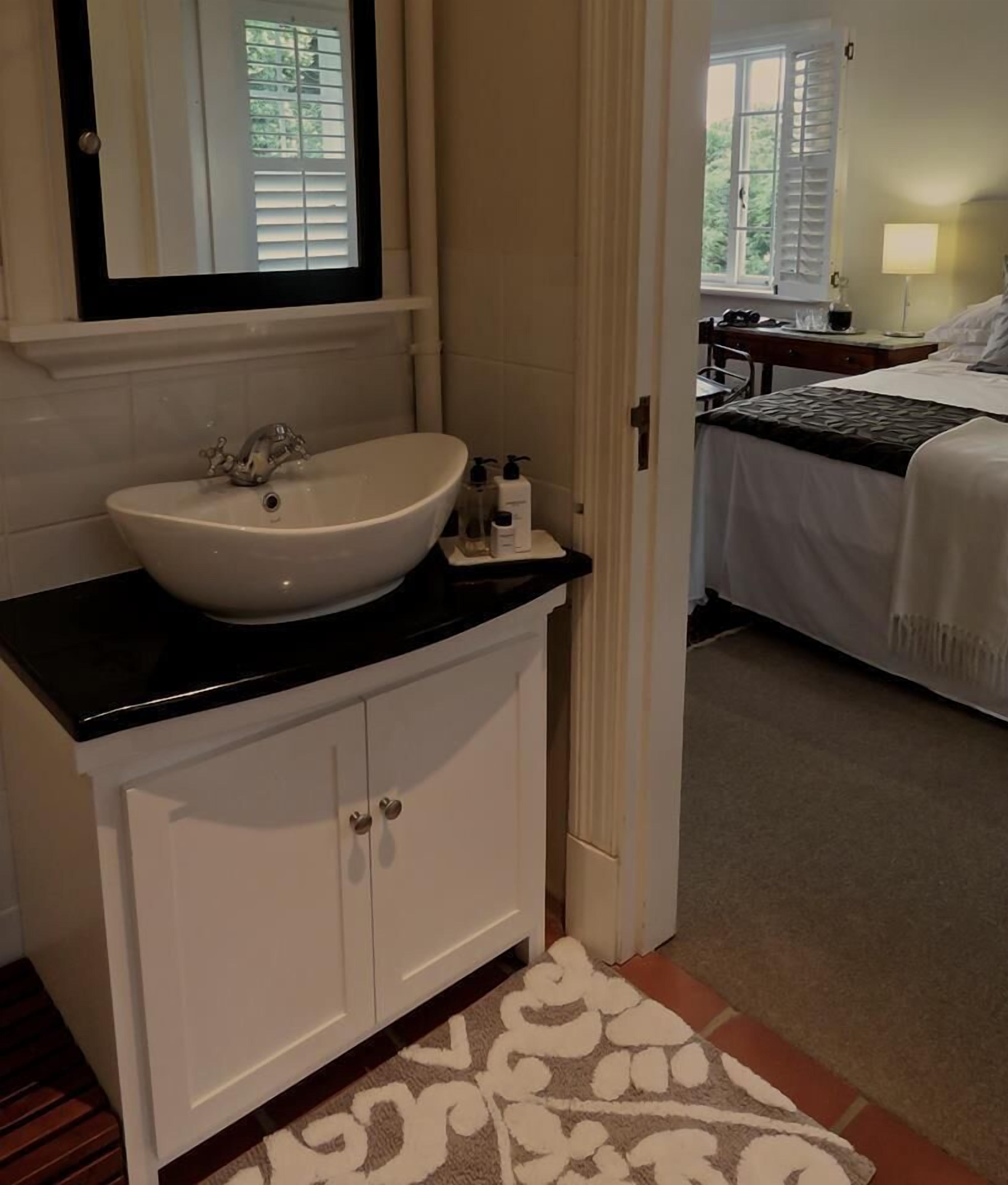 Een badkamer met een witte wastafel, een zwart aanrecht en een spiegel erboven.
