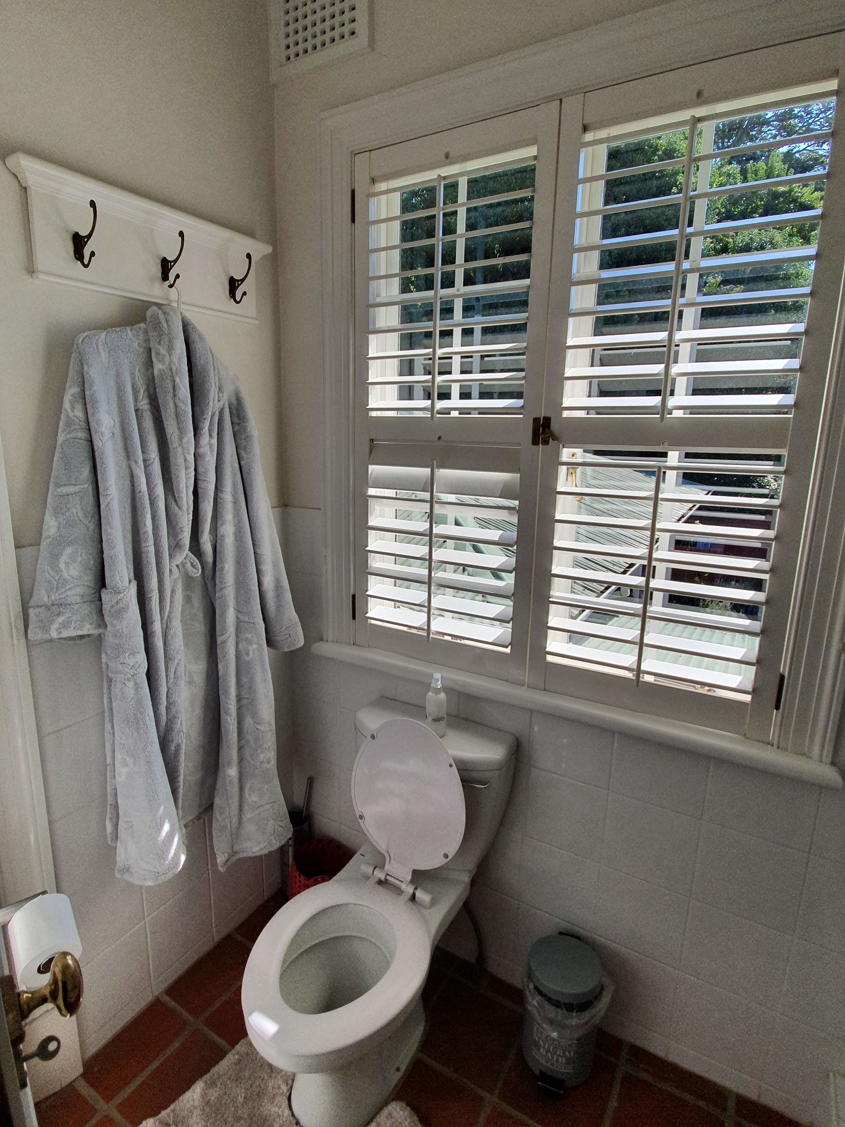 Um banheiro com vaso sanitário, janela com persianas, porta-toalhas com toalhas e lixeira.