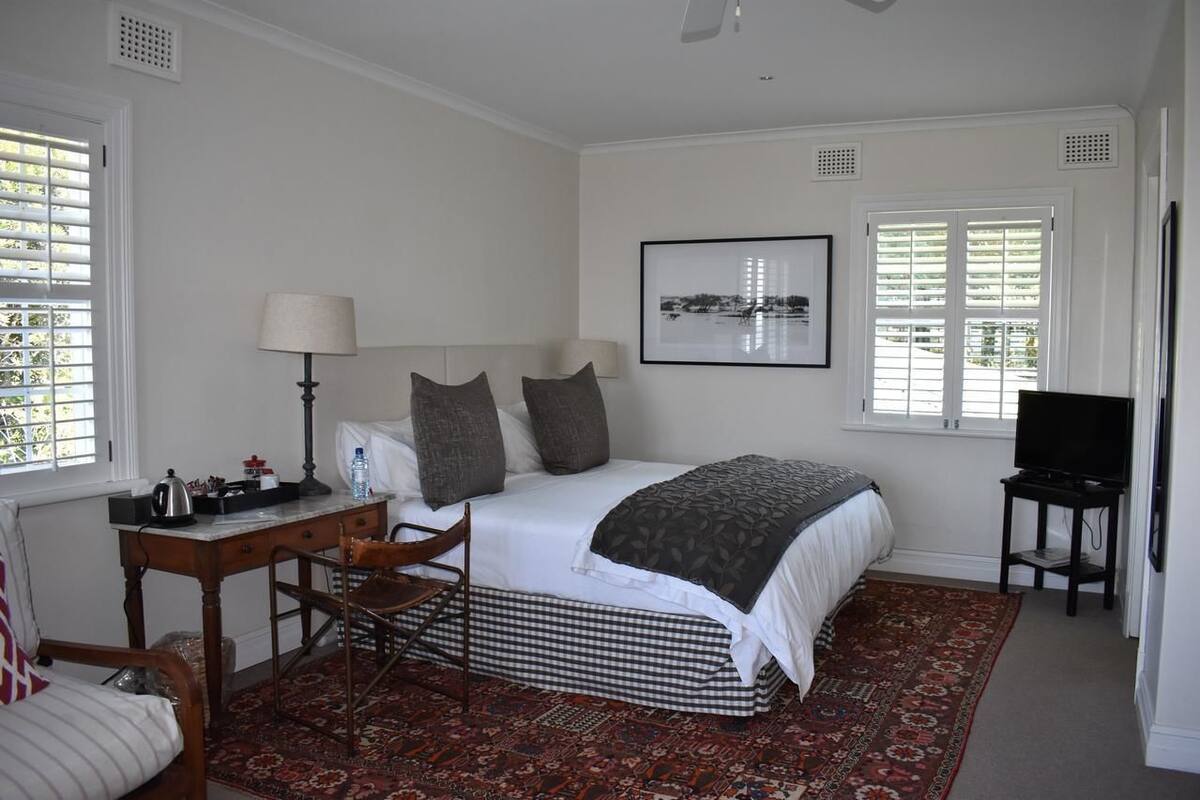 A bedroom with a bed, a desk, a chair, a television, and a window with shutters.