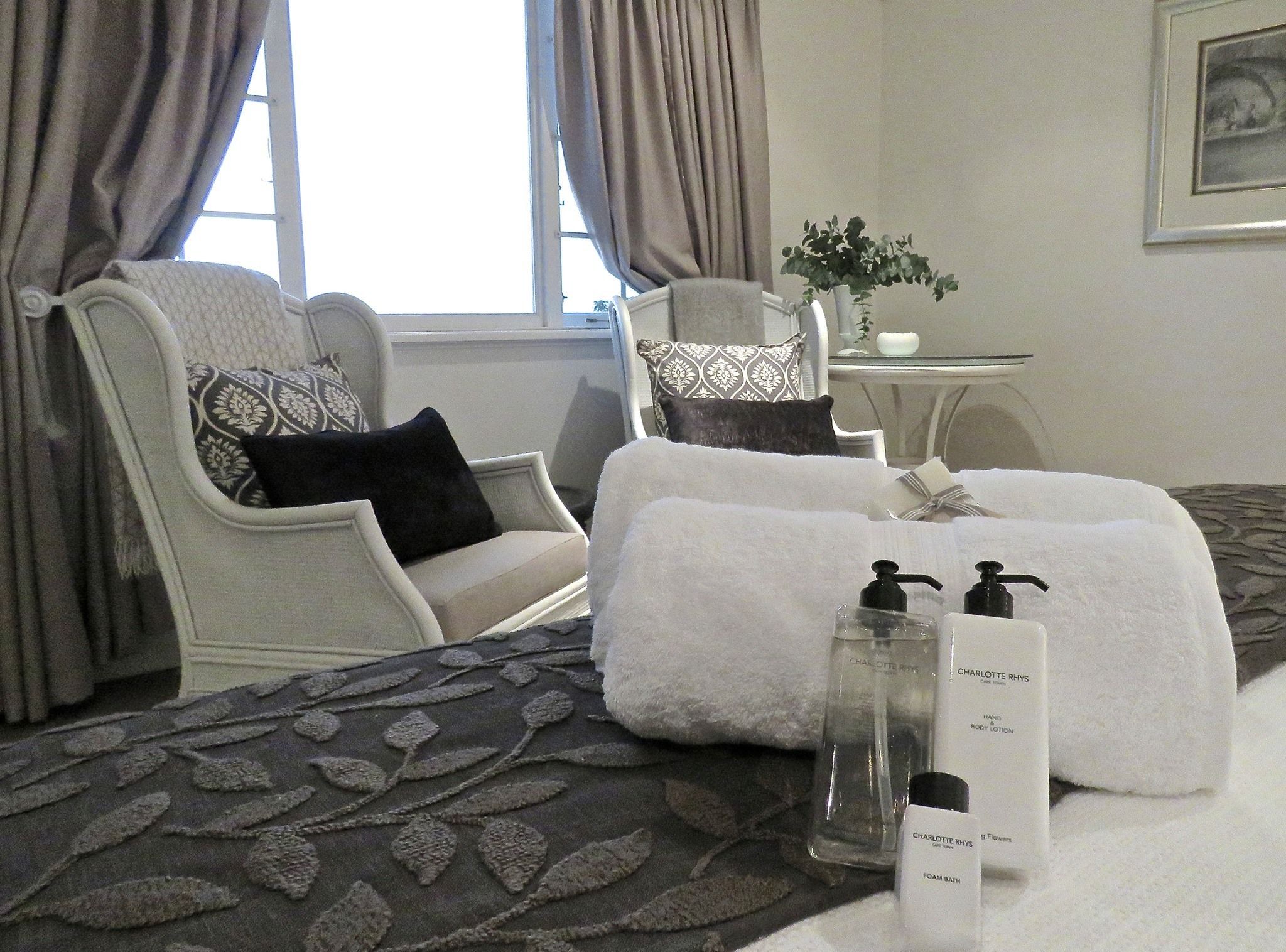 A hotel room with a bed, two chairs, a small table, and a window with curtains.