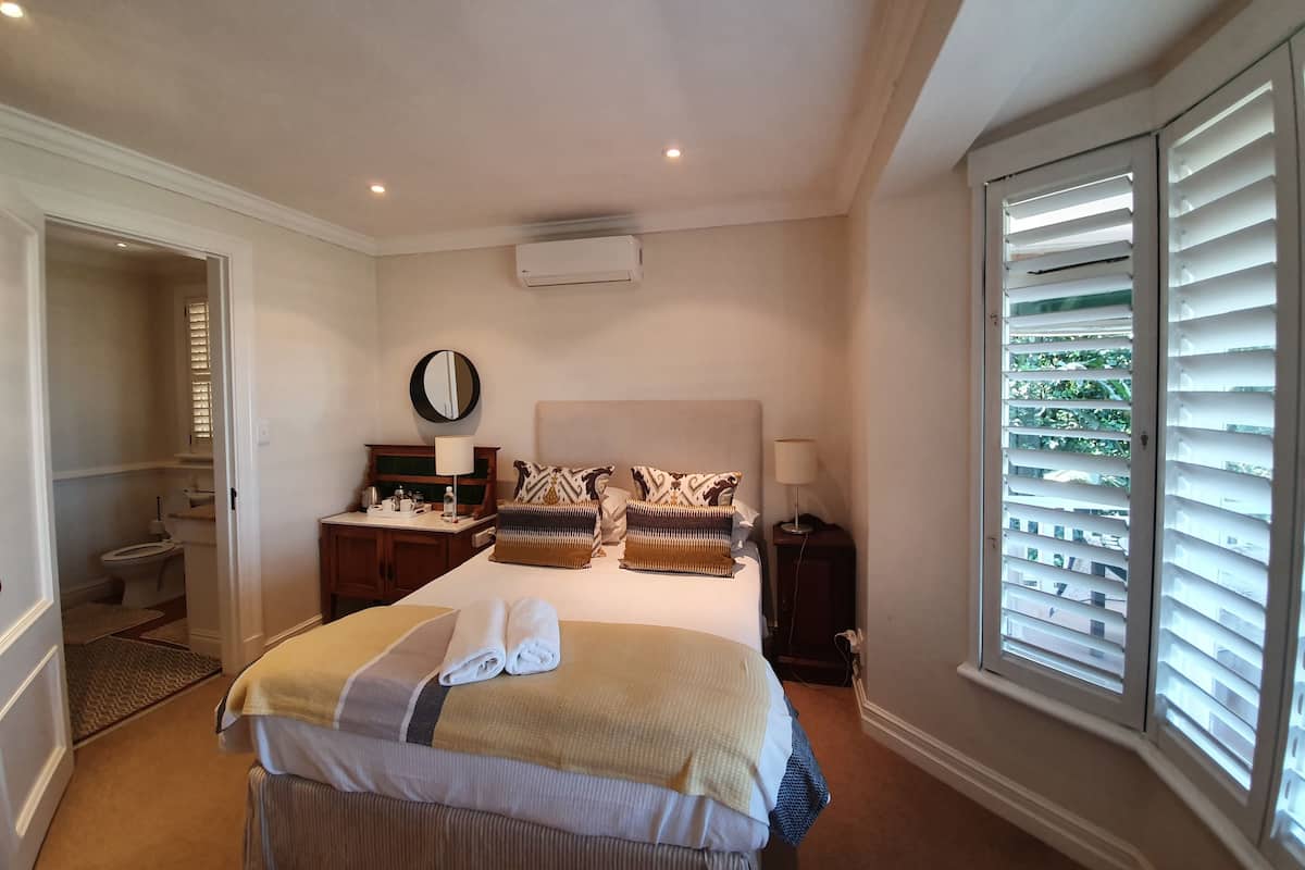 A hotel room with a bed, bedside tables, a mirror, and a window with blinds.