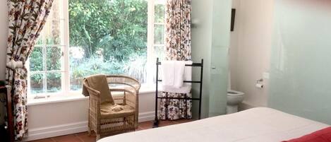 A bedroom with a bed, a chair, a window with curtains, and a toilet.