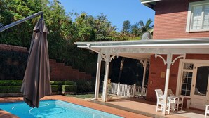 A swimming pool with a pergola and chairs, surrounded by a brick patio and a white fence. - Southey House (Kloof)