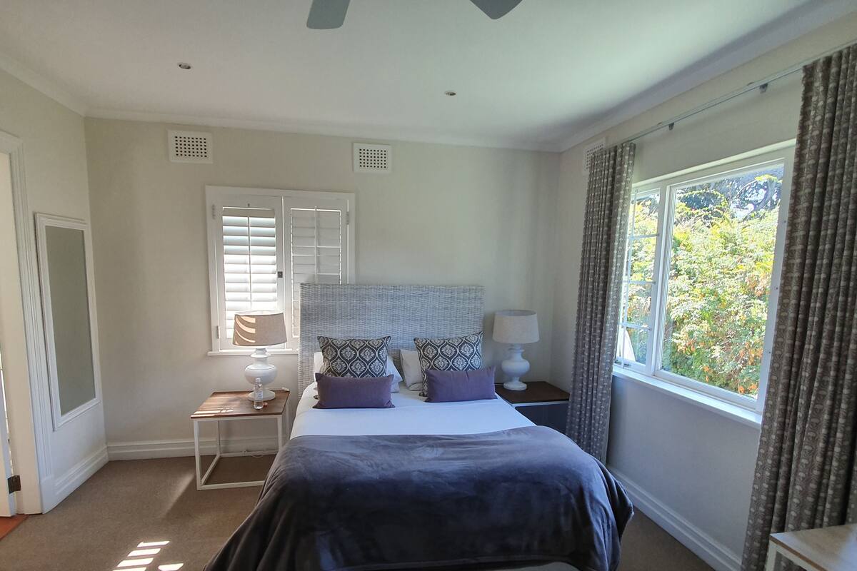 A bedroom with a bed, two bedside tables, a window with curtains, and a door.