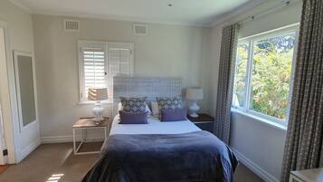 Un dormitorio con una cama, dos mesitas de noche, una ventana con cortinas y una puerta.