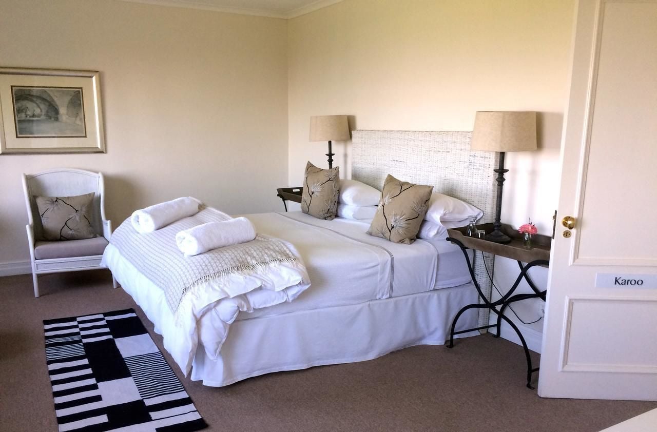 A neatly arranged bedroom with a bed, two bedside tables, a chair, and a door labeled "Karoo".