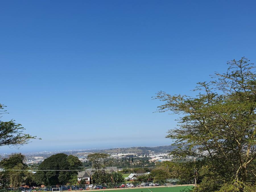 A view of a sports field with a fence, trees, and buildings in the background.
