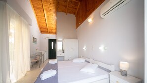 A hotel room with a large bed, bedside table with a lamp, a desk with a chair, and a bathroom visible through an open door. - Xi Village (Kefalonia)