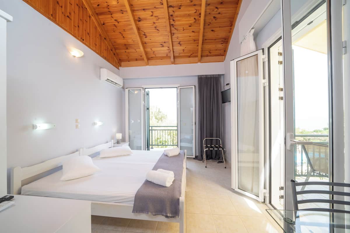 A hotel room with two beds, a balcony with a chair, and a TV on the wall.