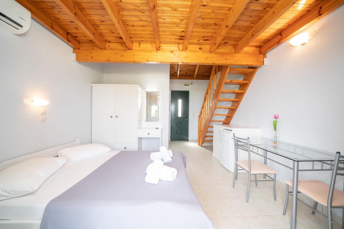 A bedroom with a bed, a desk, and a chair. There is a staircase leading to an upper level.