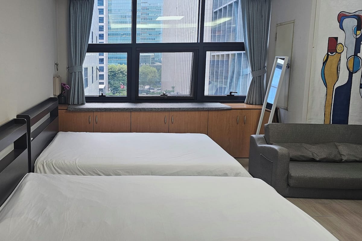 A hotel room with two beds, a window with curtains, a sofa, and a painting on the wall.