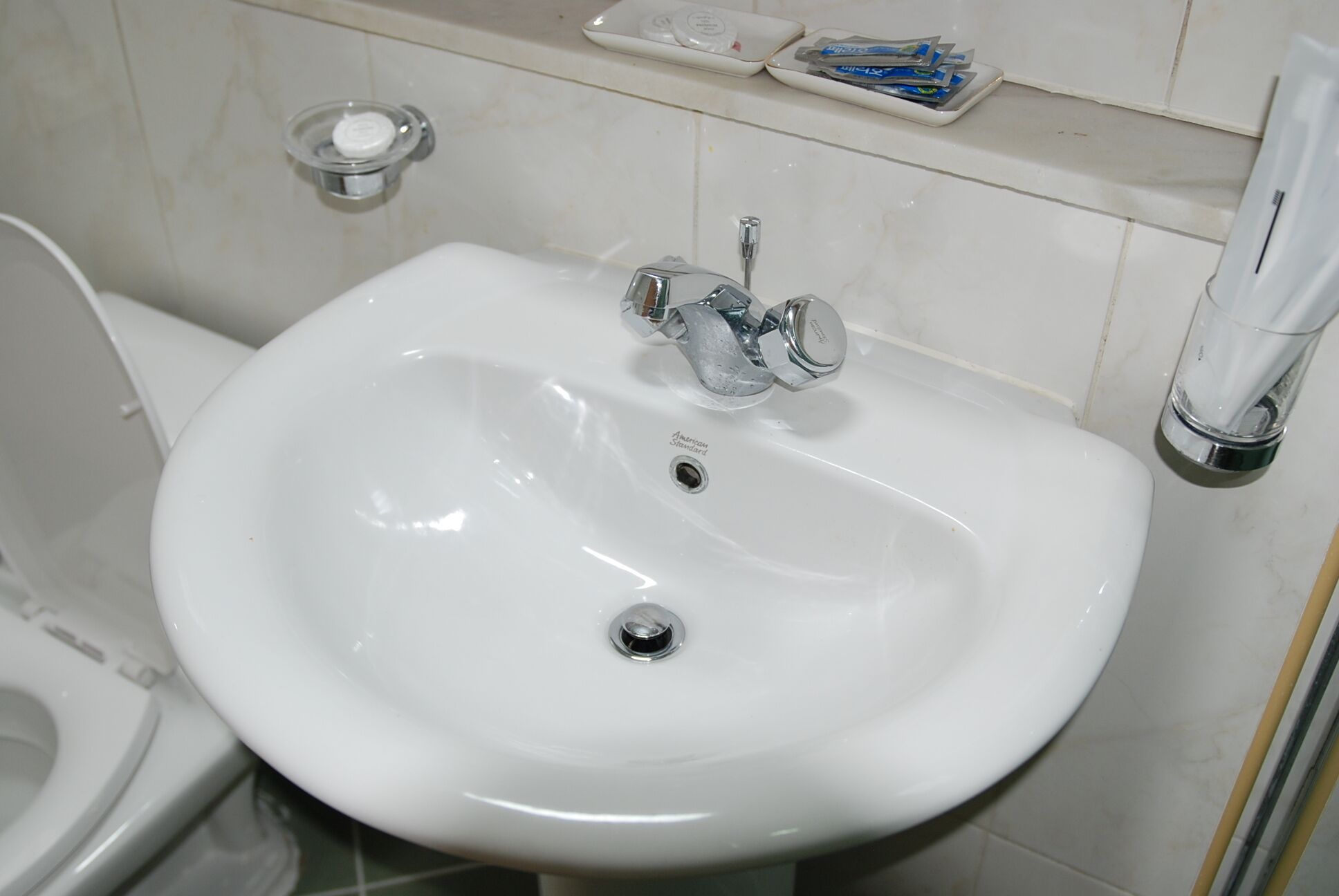 Un lavabo bianco con rubinetto cromato, un portapiatti per sapone e uno scafo WC sullo sfondo.