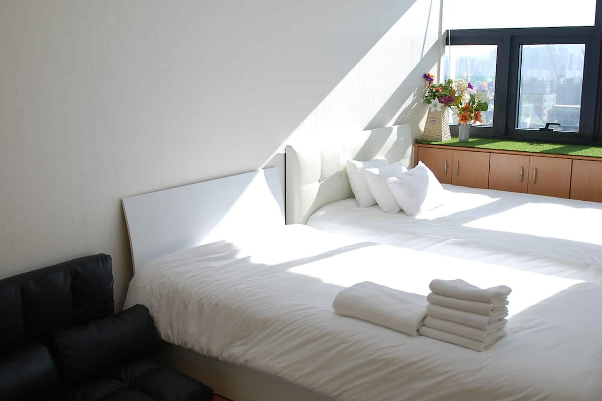 A modern hotel room with a large bed, a dark sofa, and a window with a city view.