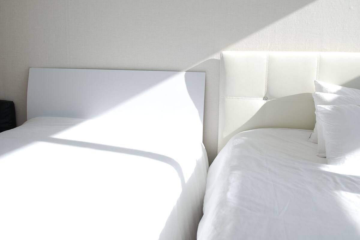 A hotel room with two beds, one with a headboard and one without, and a nightstand.