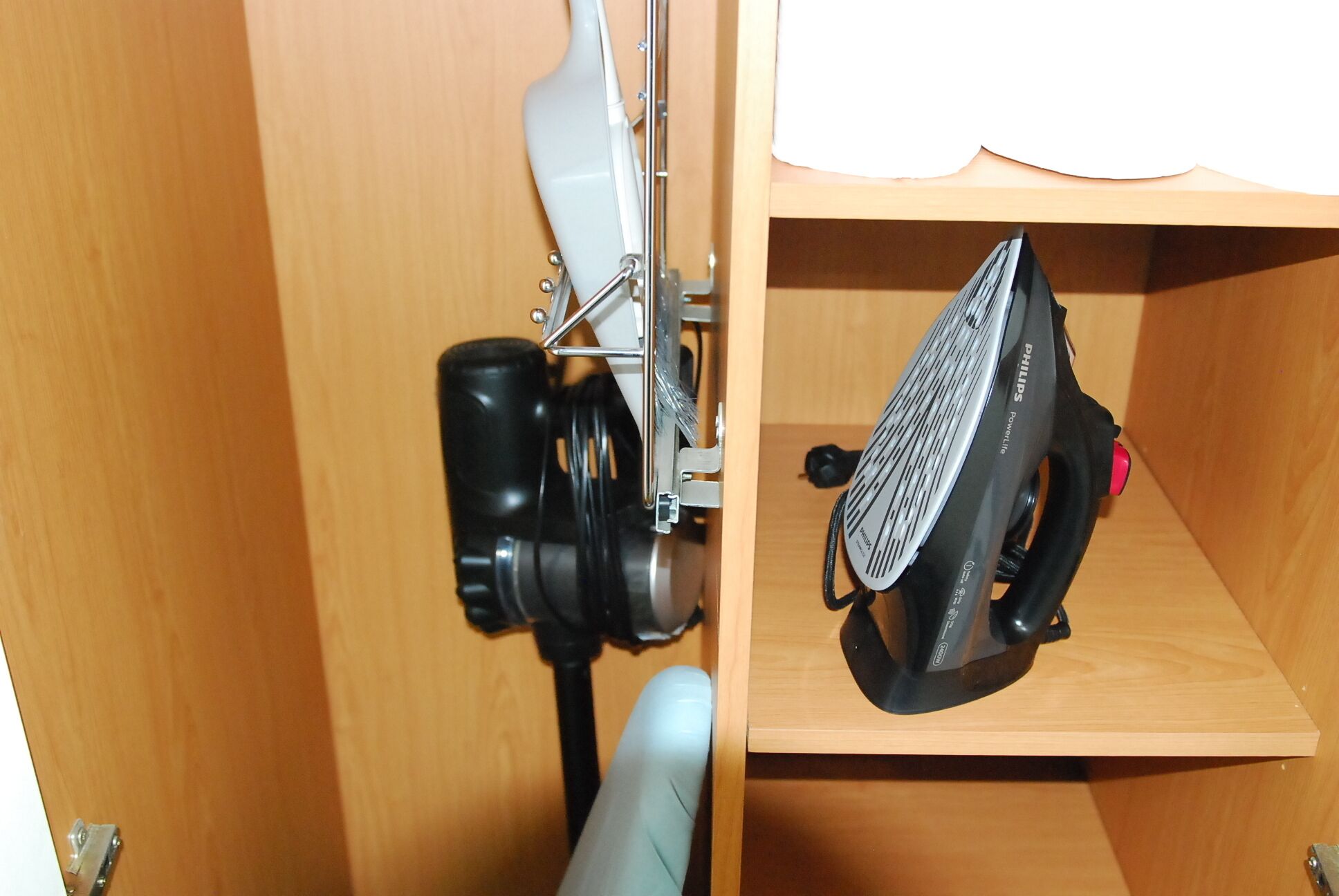 A wooden cabinet with a shelf containing a black hairdryer and a white device, possibly a hair straightener.