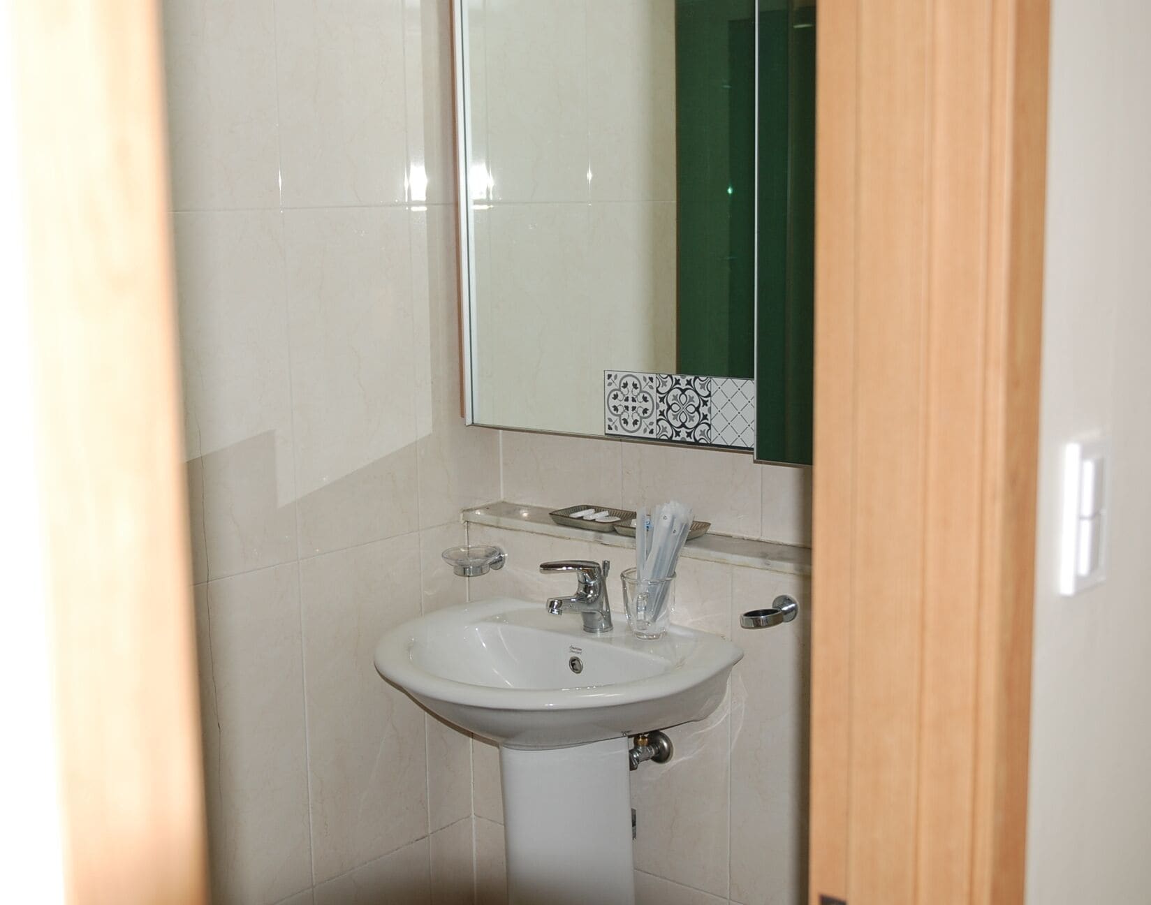A bathroom with a white sink, a mirror, and a green-tiled wall.