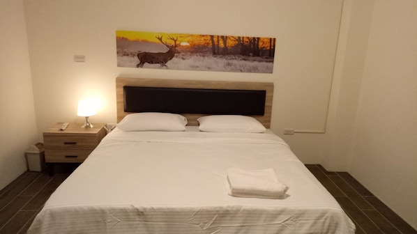 A neatly made bed with a white bedspread and pillows, a wooden nightstand with a lamp, and a painting of a deer on the wall. - Yuanshan Dahu Homestay (Yuanshan)