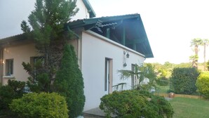 A house with a white exterior, a sloped roof, and a small porch area. - House with garden, close to the beach, the port and the river shuttle (boucau)