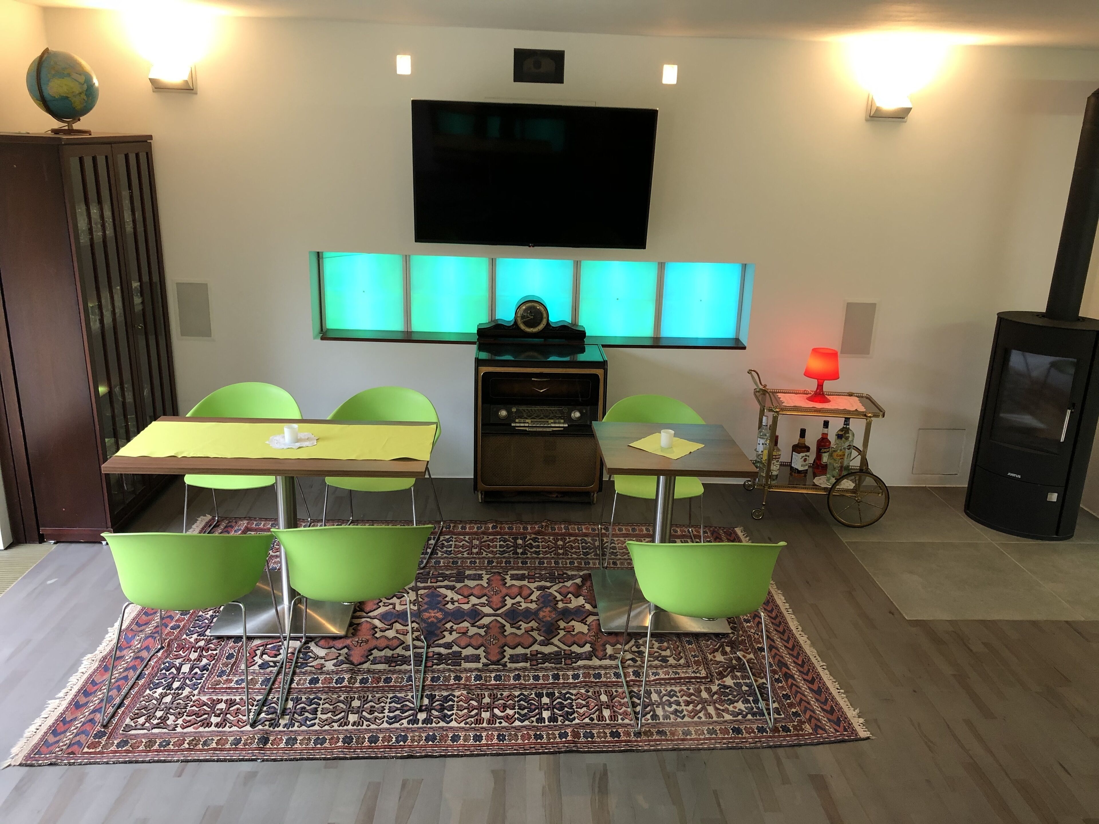 Ein modernes Wohnzimmer mit Fernseher, einem kleinen Tisch mit Stühlen, einem Vintage-Radio und einem kleinen Wagen mit Flaschen.