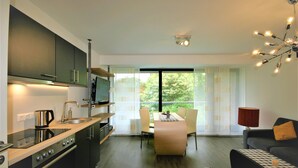 A modern kitchen with a dining area, large windows, and a view of greenery. - Schacht34 (Oberhausen)