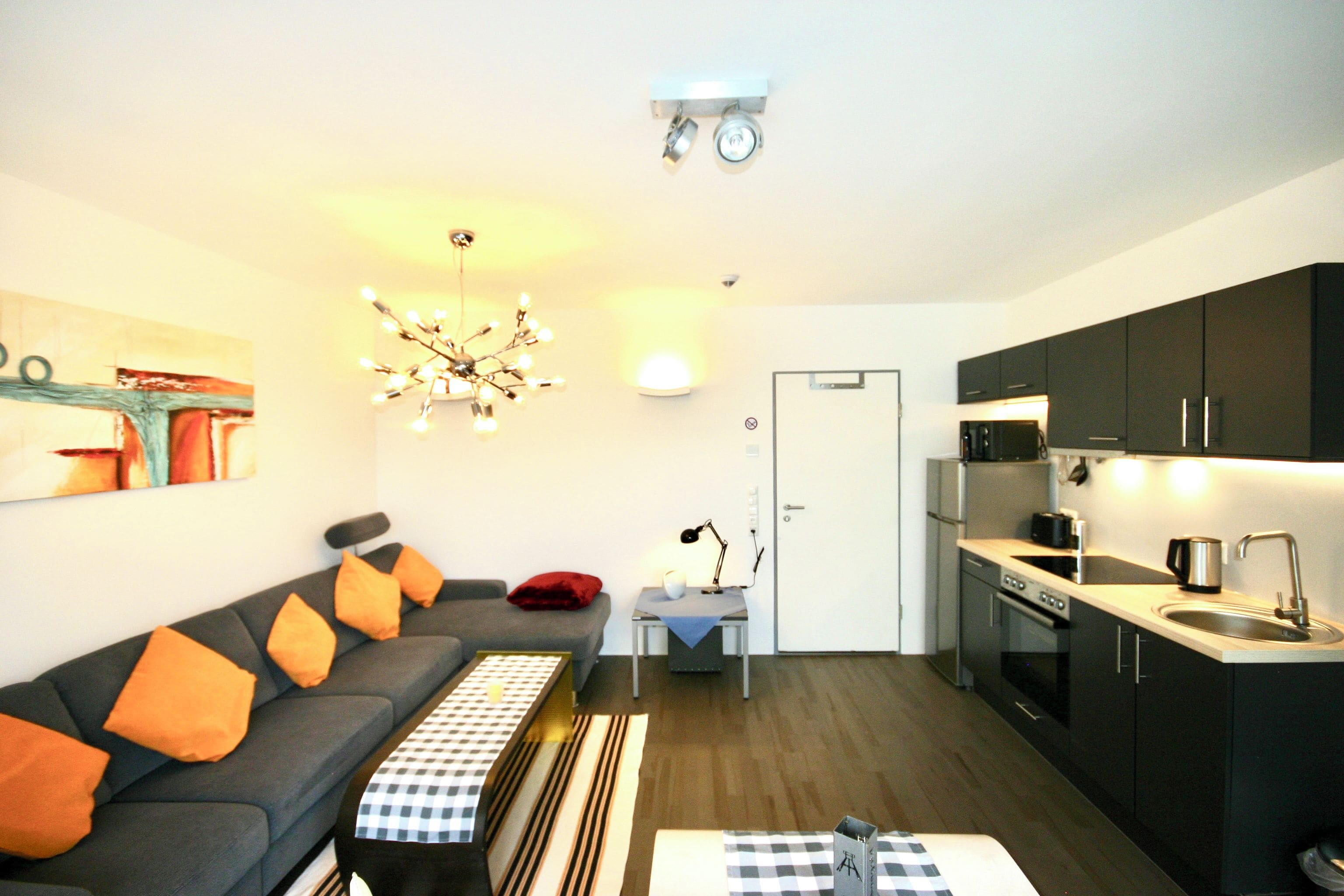 A compact living space with a sofa, a dining table, a kitchen area, and a ceiling light fixture.