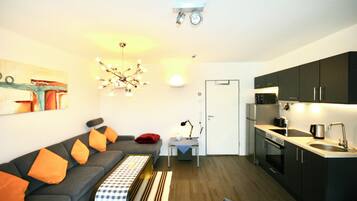 A compact living space with a sofa, a dining table, a kitchen area, and a ceiling light fixture.
