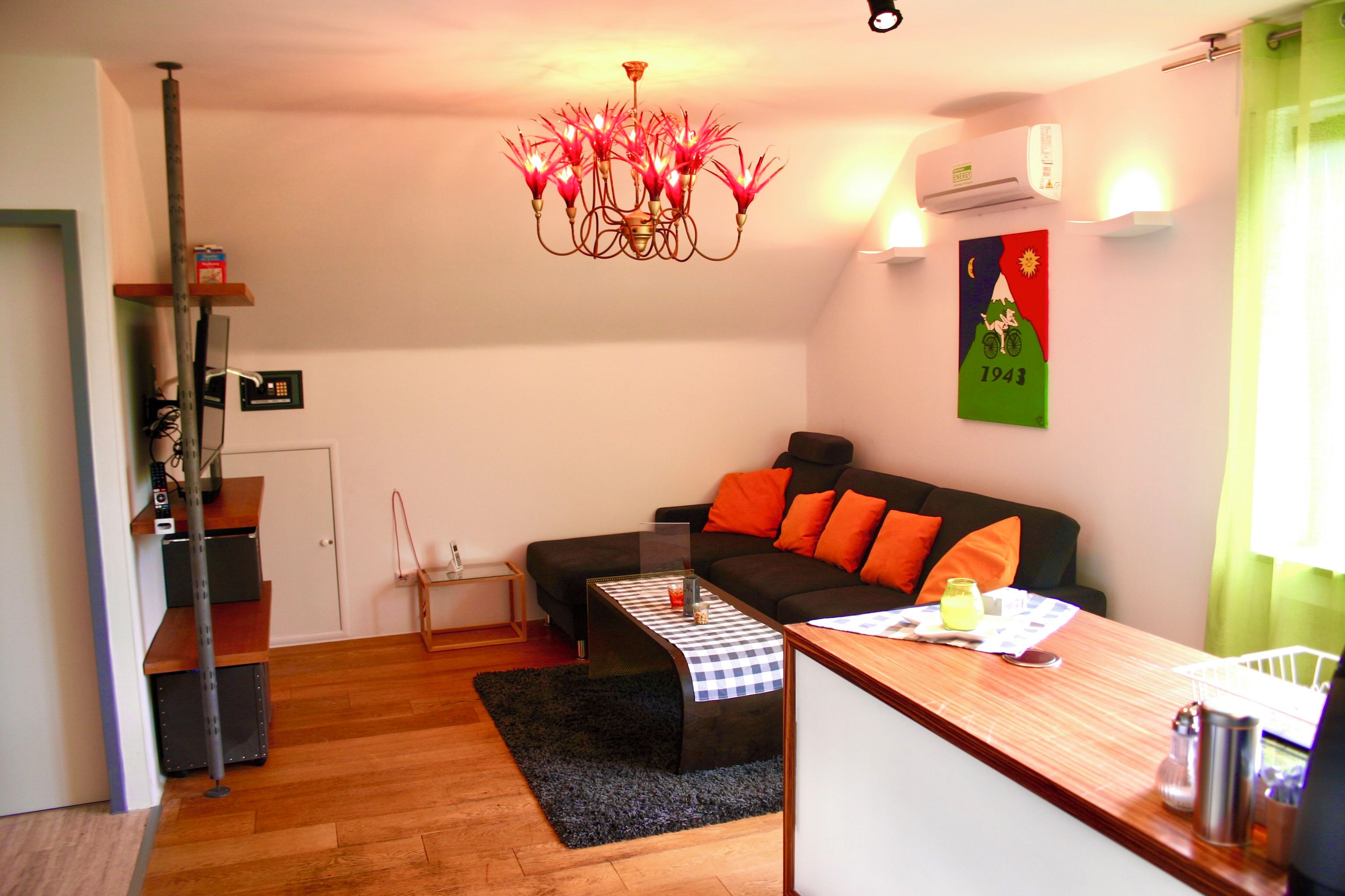 A modern living room with a black sofa, orange cushions, a wooden coffee table, and a chandelier.