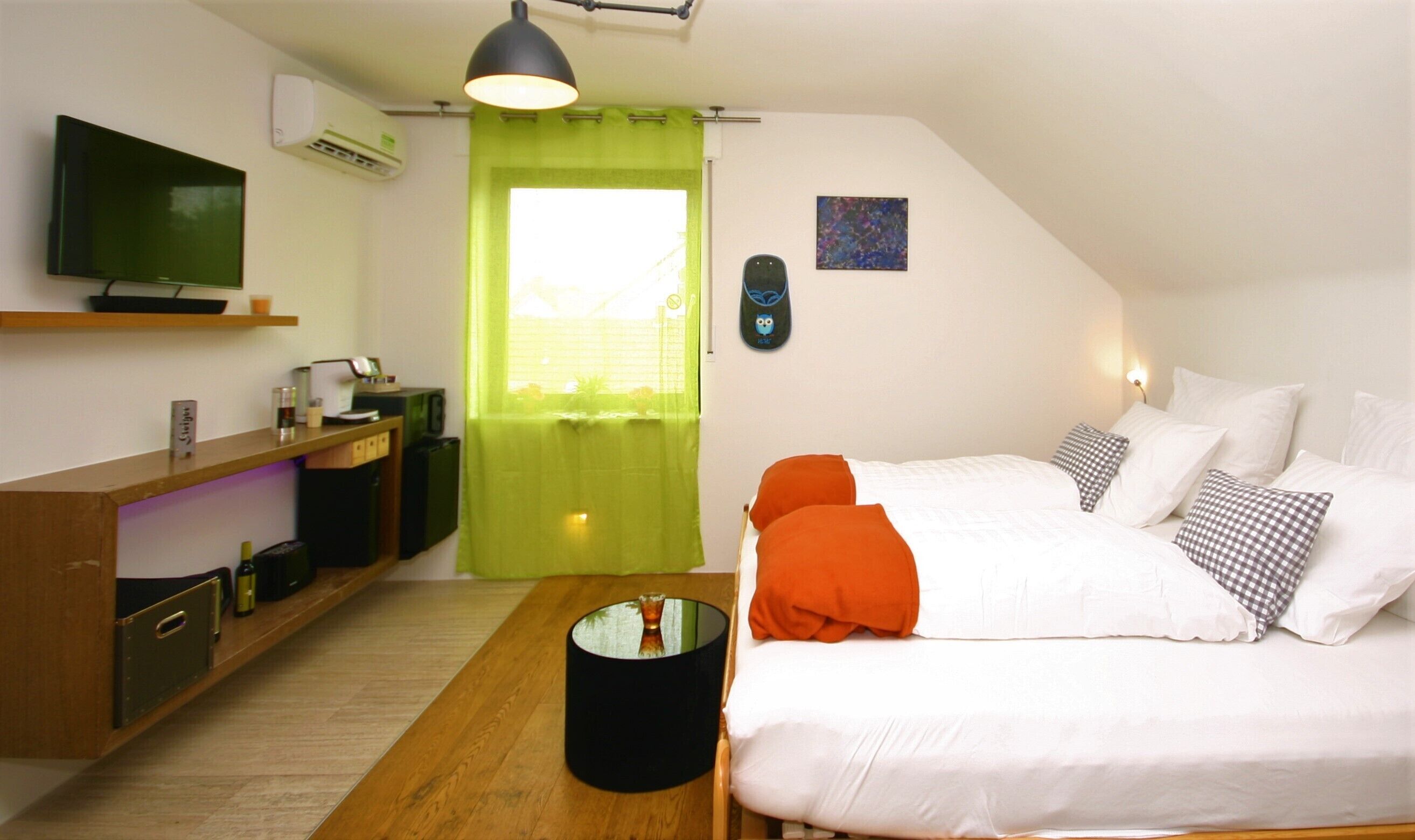 Una habitación moderna con una cama, un escritorio, un televisor y una ventana con cortinas verdes.