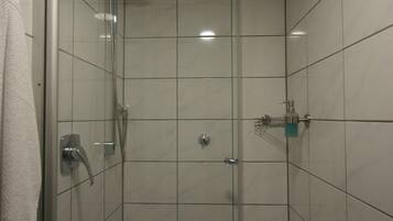 Cabina de ducha con paredes de vidrio, un cabezal de ducha de mano, un grifo de pared y un dispensador de jabón.