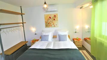 A bedroom with a bed, two bedside tables, a hanging light fixture, a wall-mounted air conditioner, and a green curtain.